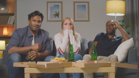 Frustrated-Multi-Cultural-Friends-Watching-Sports-Game-On-TV-Sitting-On-Sofa-At-Home-Eating-Pizza